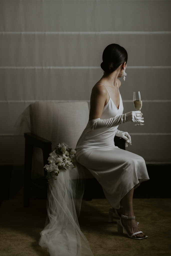 A woman in a white dress sitting on a chair holding a glass of champagne