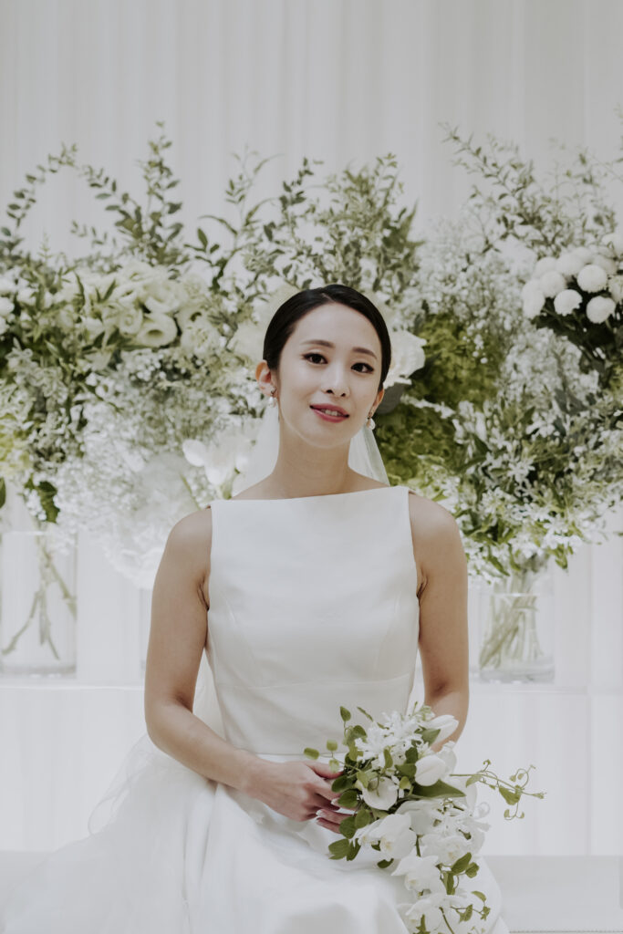 A bride in a white dress sitting in front of a white wall.