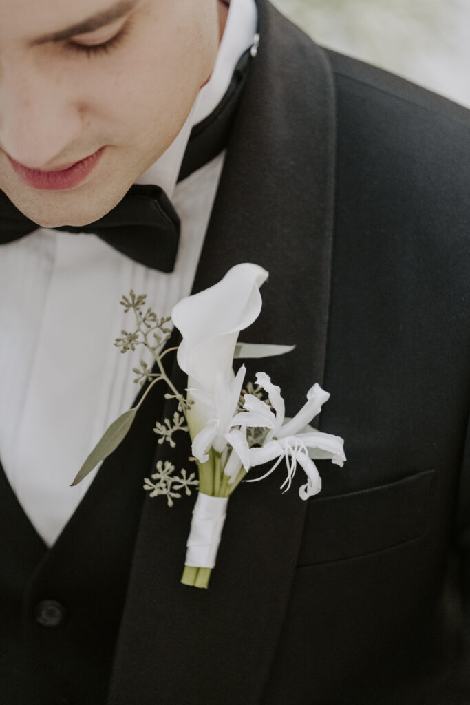 A groom in a black tuxedo wearing a white boutonniere.