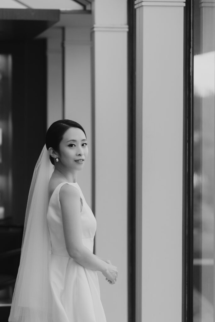 A bride in a wedding dress standing in front of a window of the Seoul Grand Hyatt Hotel.