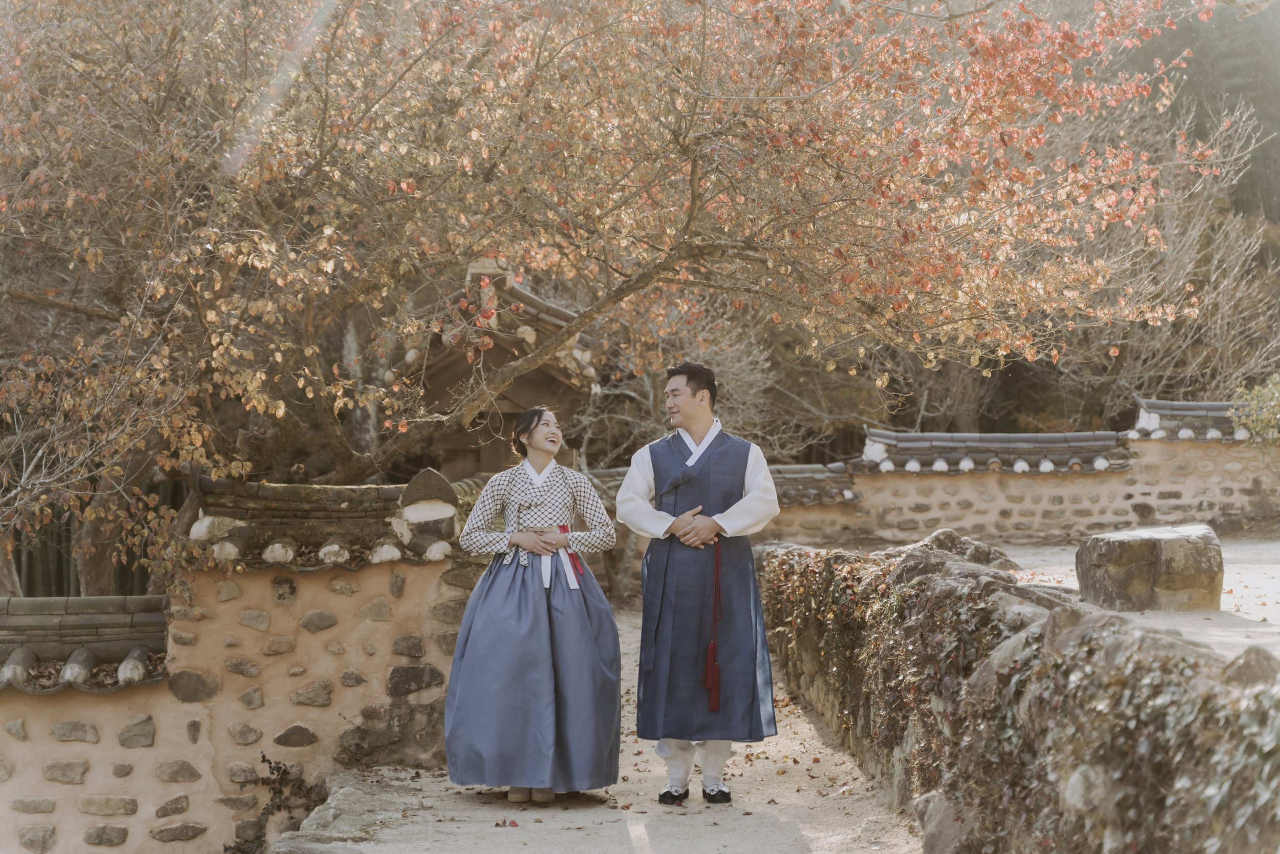 A couple in traditional korean clothing standing next to a stone wall.