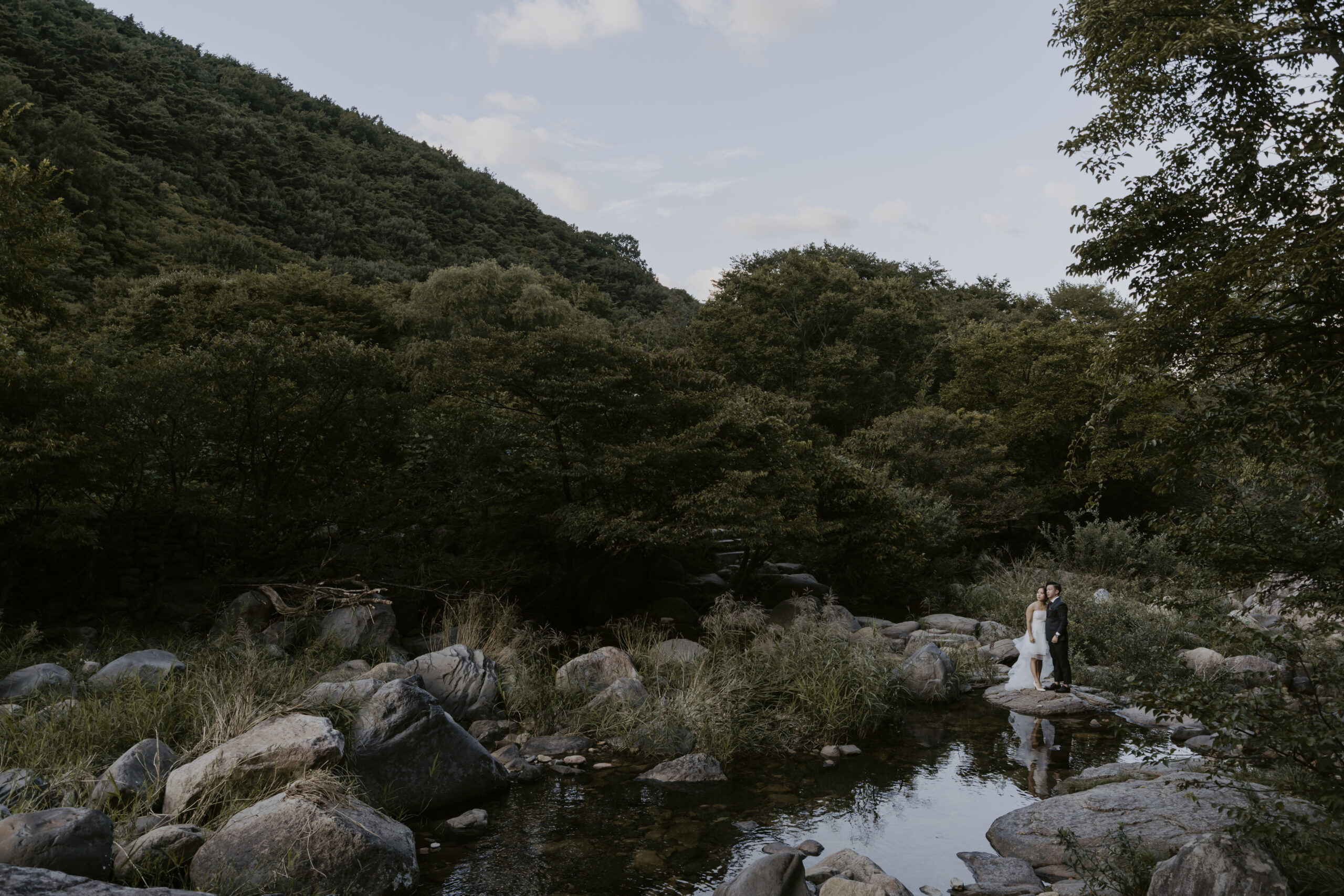 a bride and groom stand on a rock in the valley during their pre-wedding photoshoot in Korea