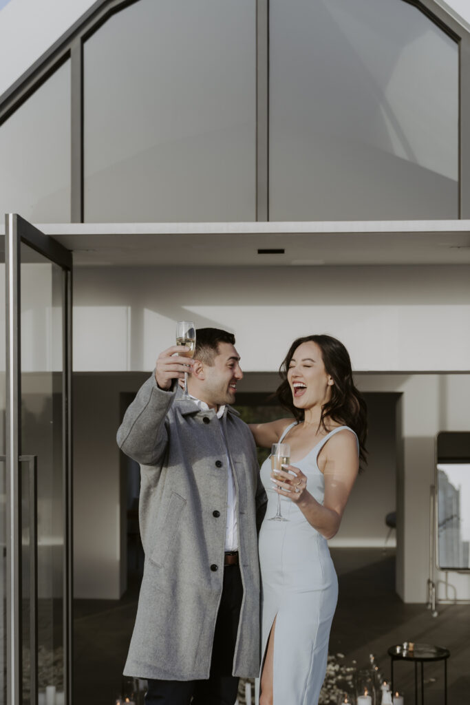 A couple holding champagne glasses in front of a building.