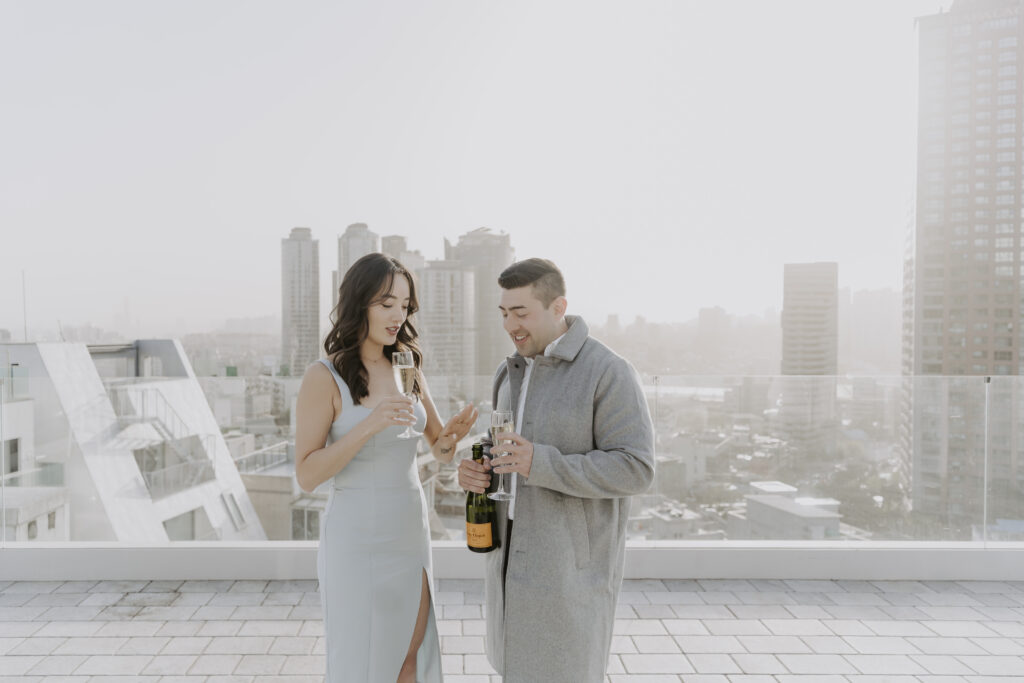 A man and woman standing on top of a rooftop with a bottle of champagne.