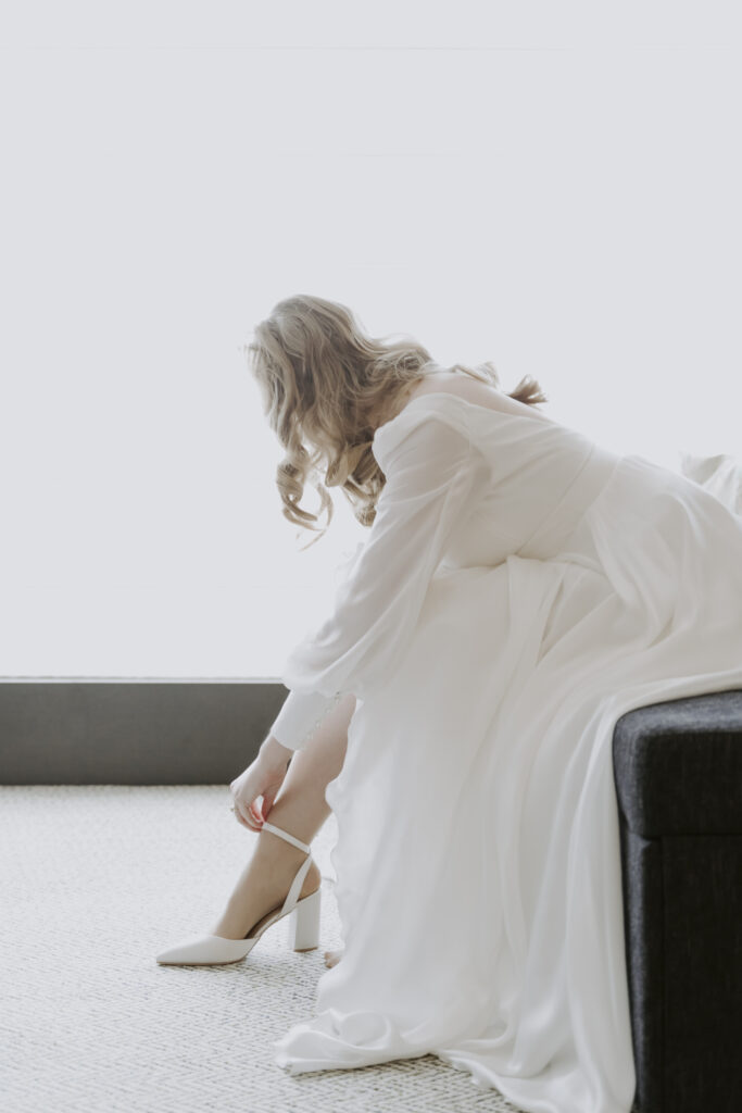 A bride in a white dress preparing for her Seoul elopement by tying her shoes.
