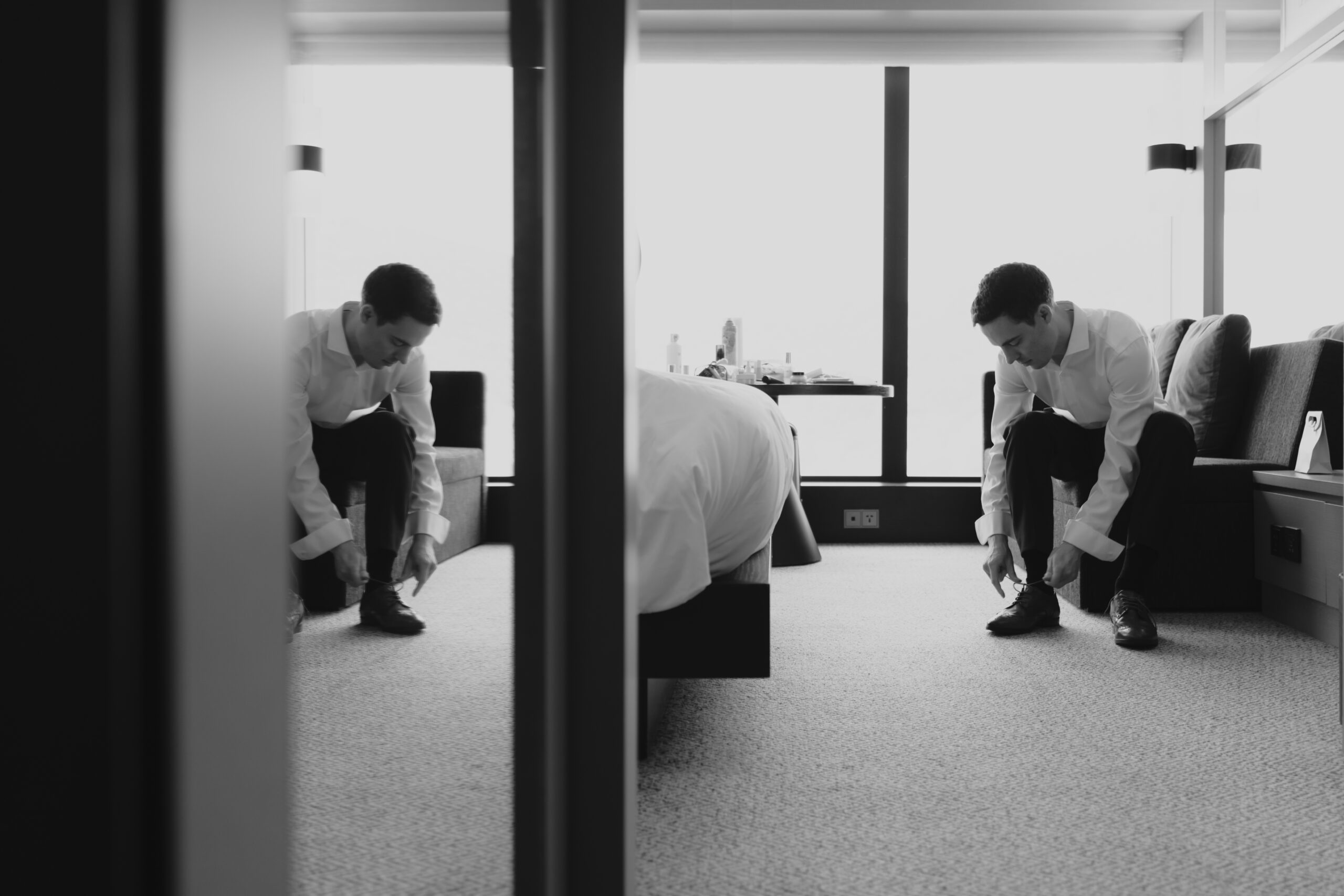 A man tying his shoes in a hotel room during a Seoul elopement.