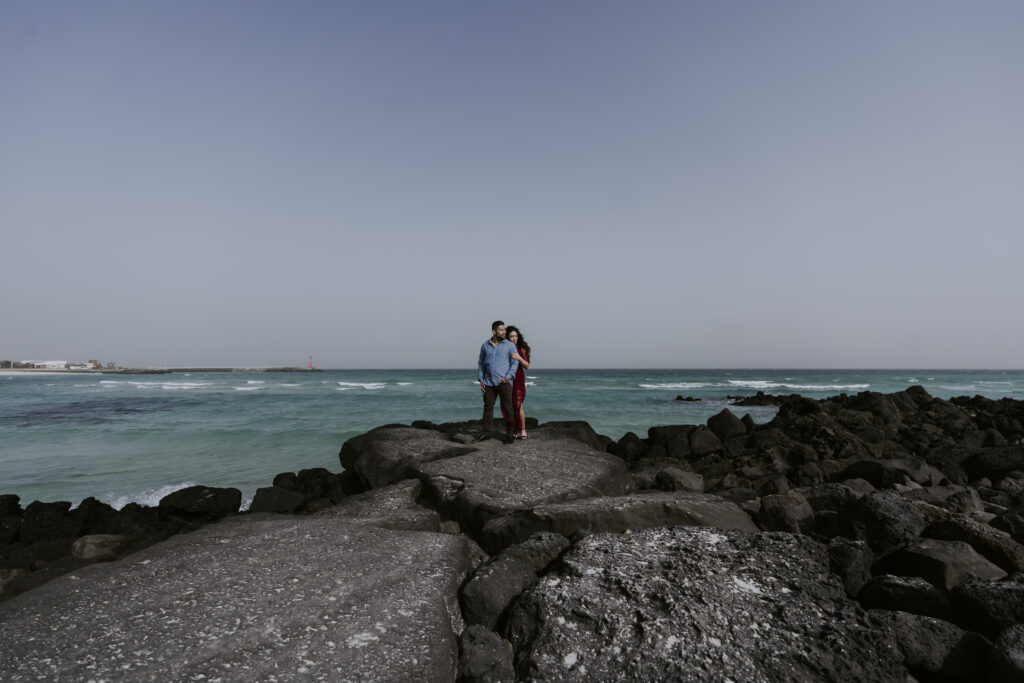 A couple standing on rocks in front of the ocean.