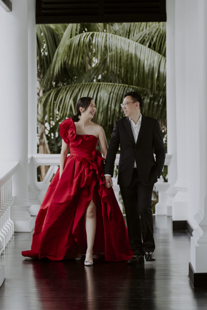 A man and woman in wedding attire walking down a hallway at Raffles Hotel Singapore.