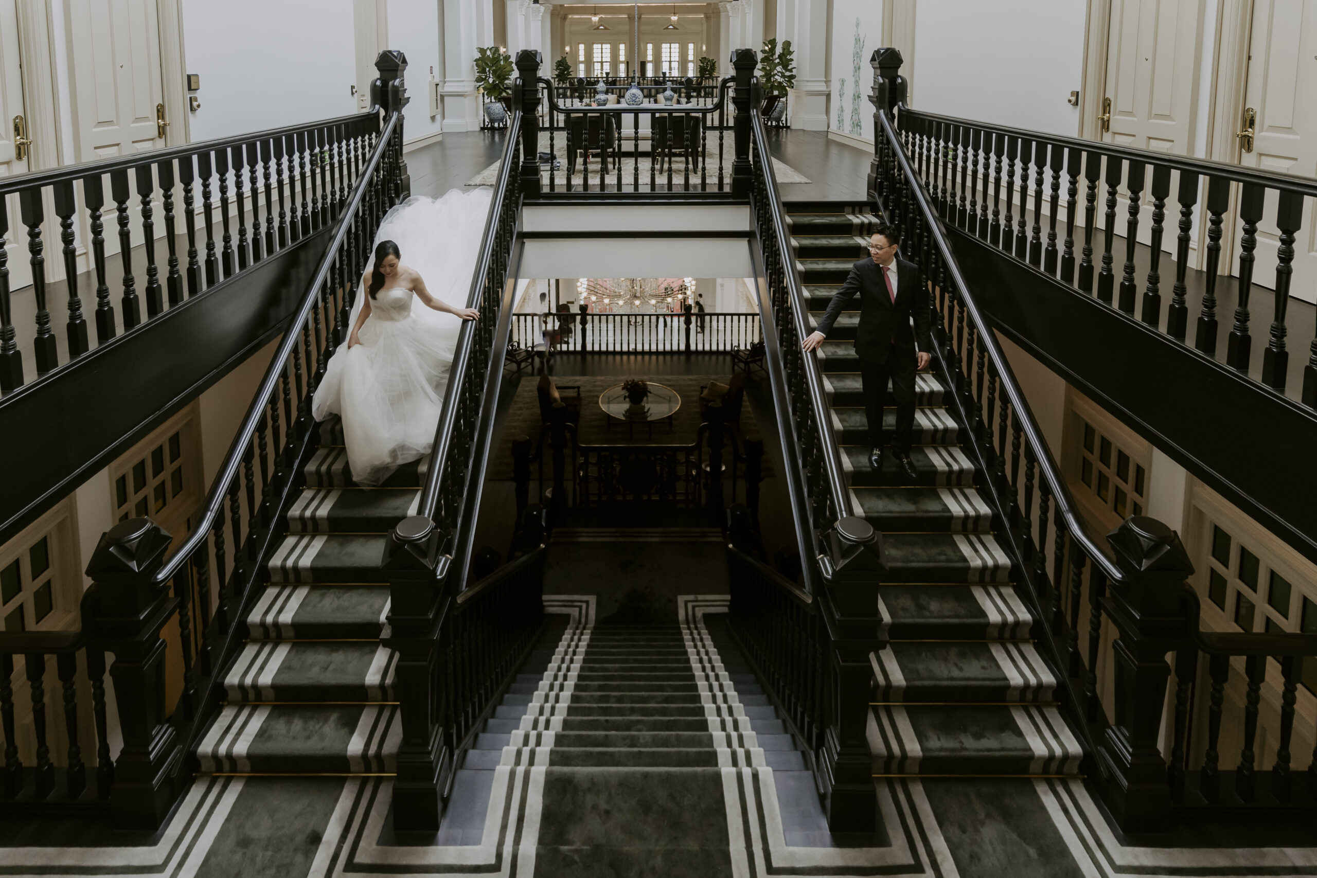 A bride and groom elegantly descending the stairs of Raffles Hotel Singapore for their wedding.