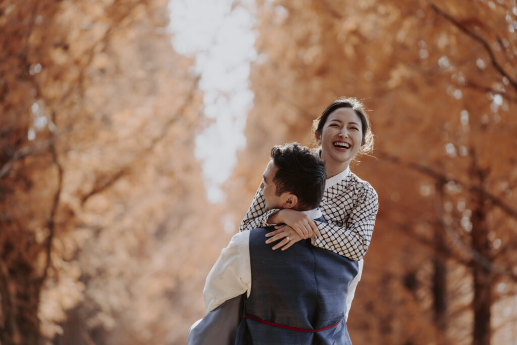 A couple embracing affectionately amidst the scenic beauty of a park in Korea, experiencing the changing seasons.