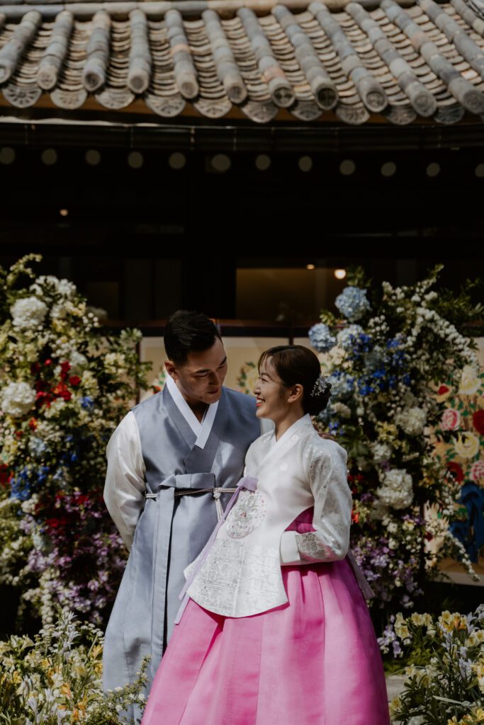 A couple in traditional korean clothing standing in front of their wedding venue in a hanok house.