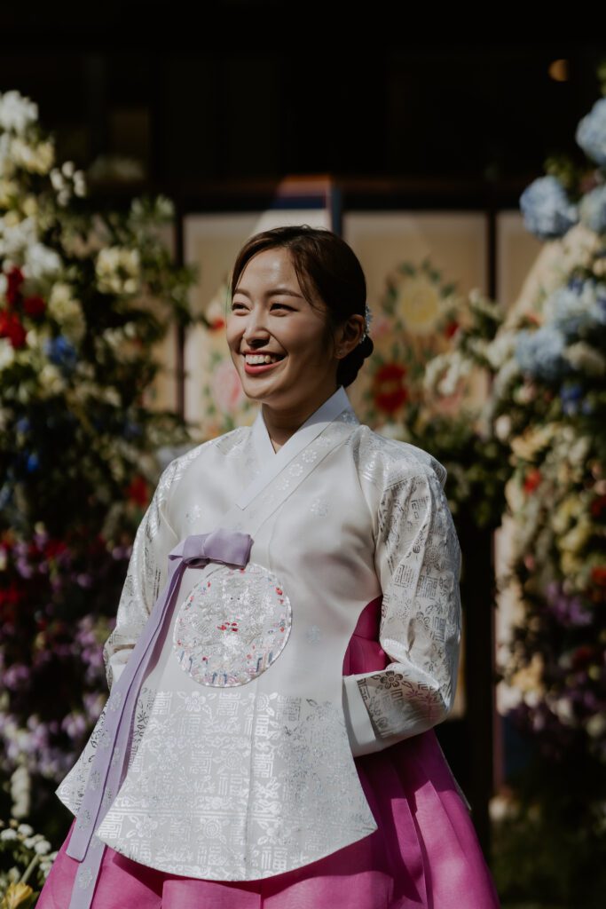 A bride in Korean hanbok dress smiles in front of flowers.