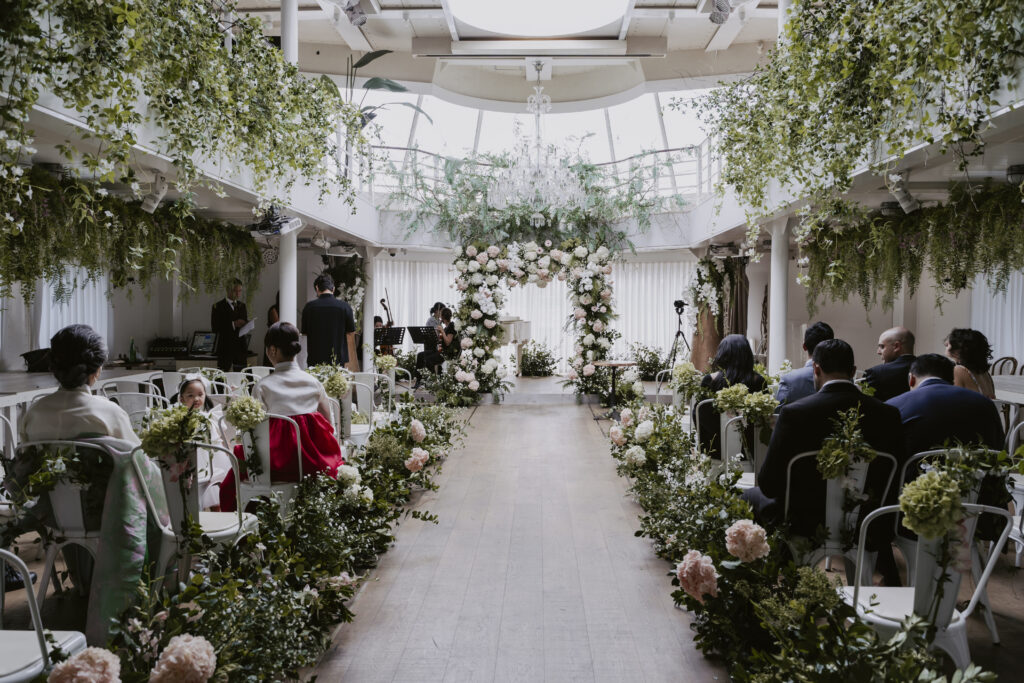 A wedding ceremony in a room filled with greenery at Ailey House Wedding Venue.