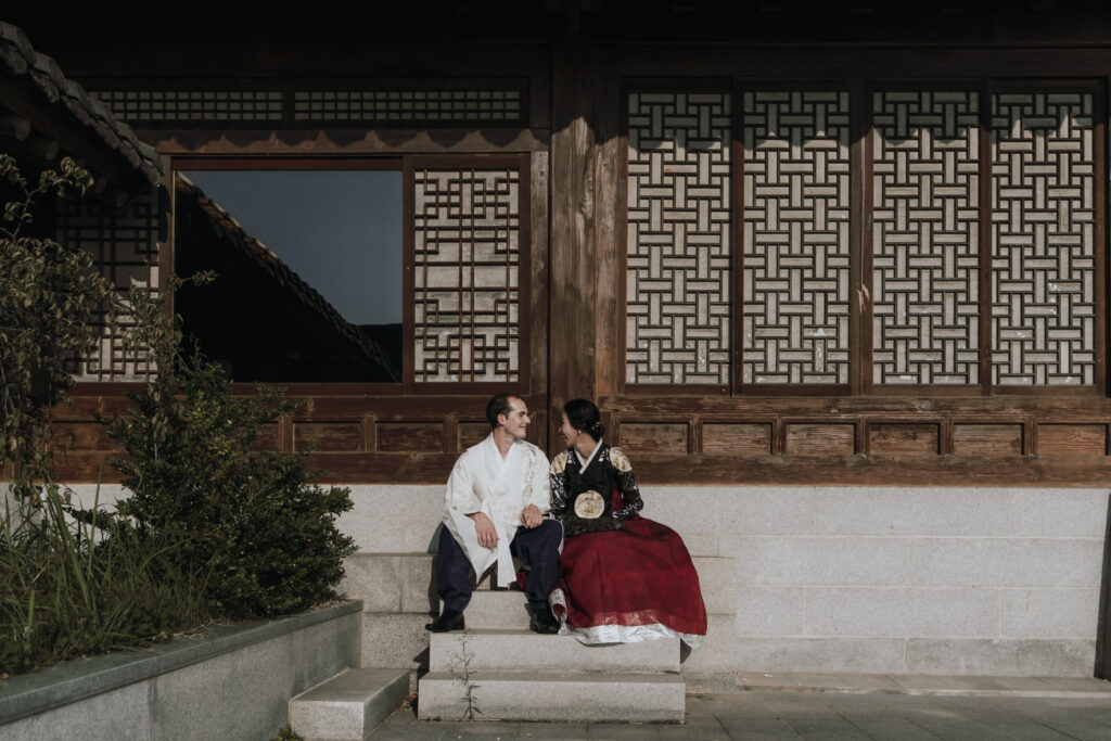 A couple in traditional korean clothing sits on the steps at a hanok house venue in Korea.