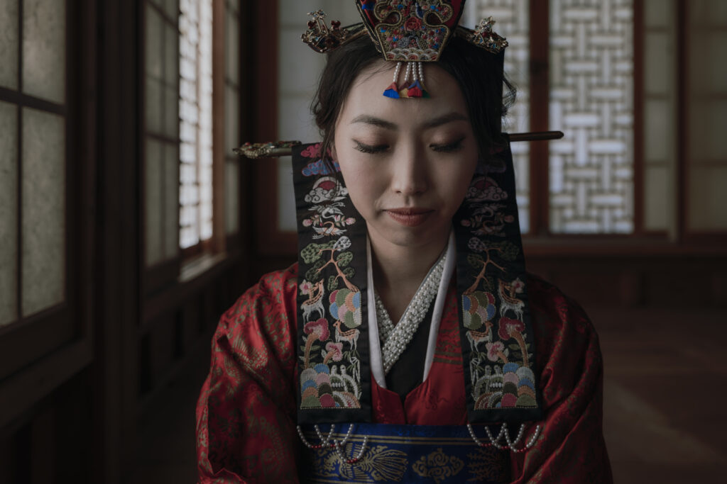 A woman in traditional korean clothing is sitting in a hanok.