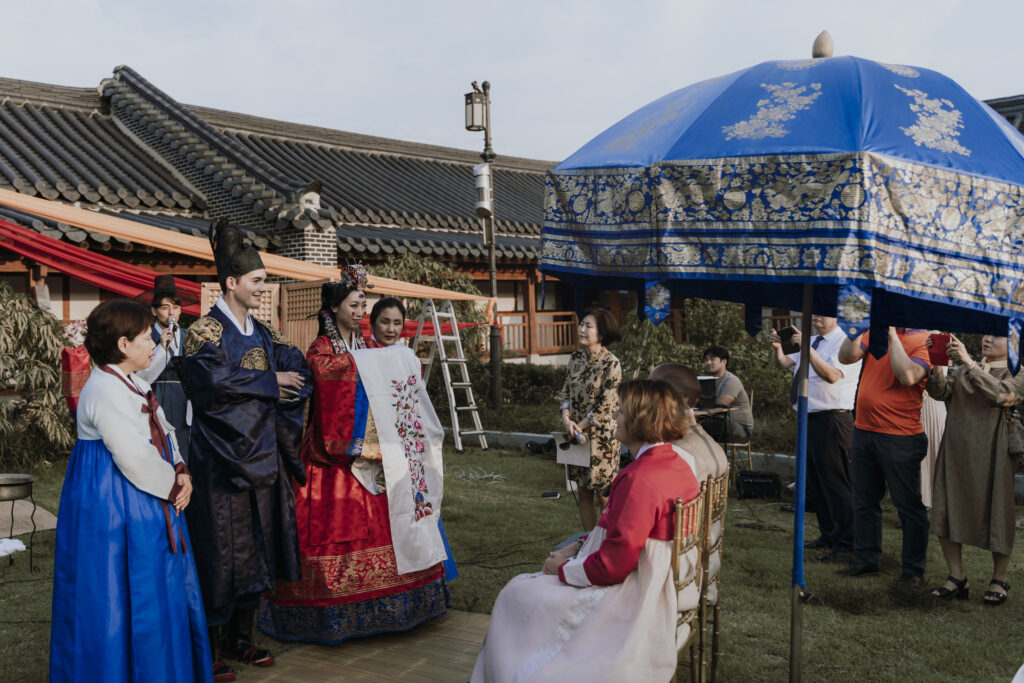 A group of people in traditional korean clothing standing under an umbrella.