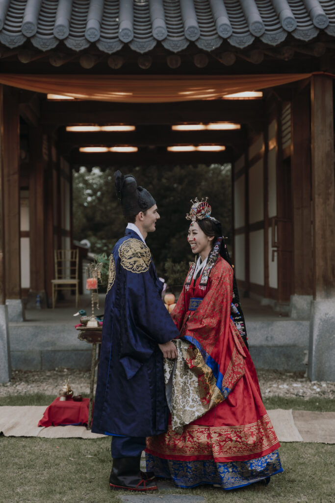 A bride and groom in traditional korean clothing standing in front of a pagoda.