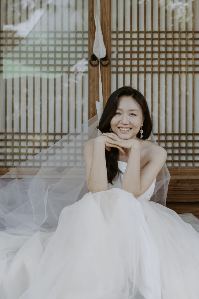 A bride in a white wedding dress sitting in front of a hanok house wedding venue.
