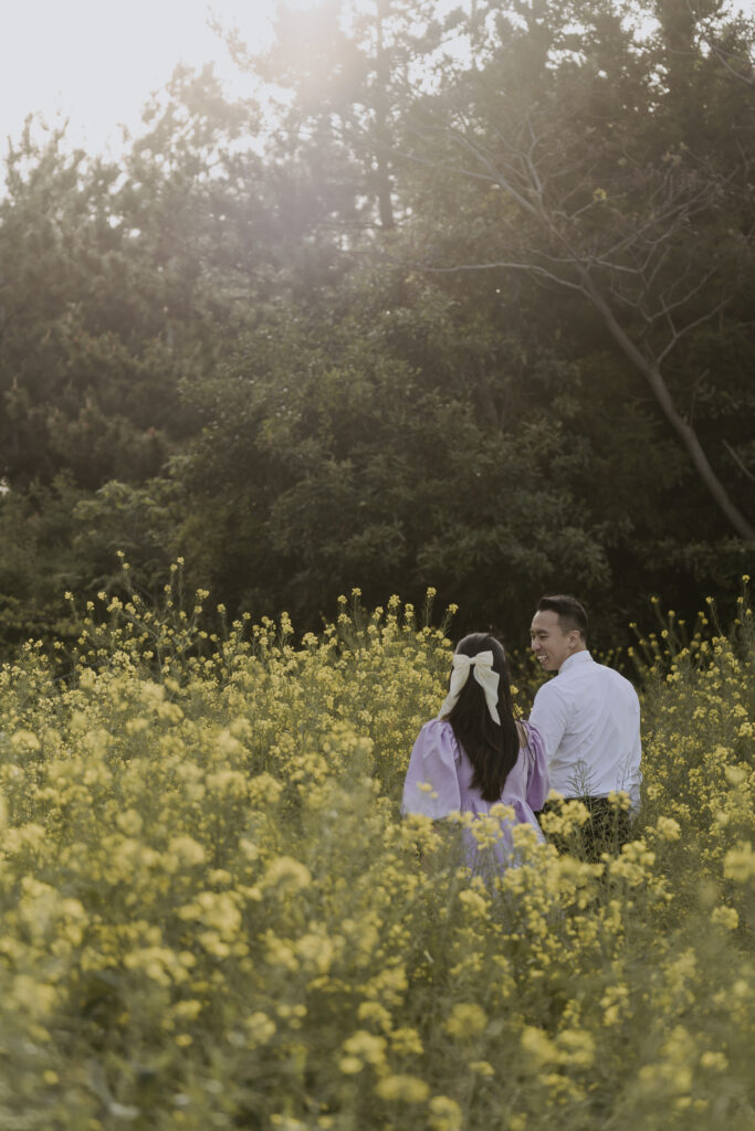 A bride and groom standing in an outdoor field of yellow flowers for their pre-wedding outdoor photoshoot
