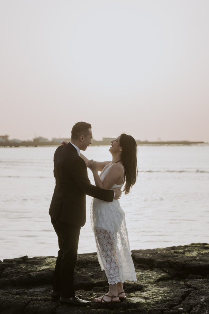 A bride and groom standing on rocks near the water during their pre-wedding