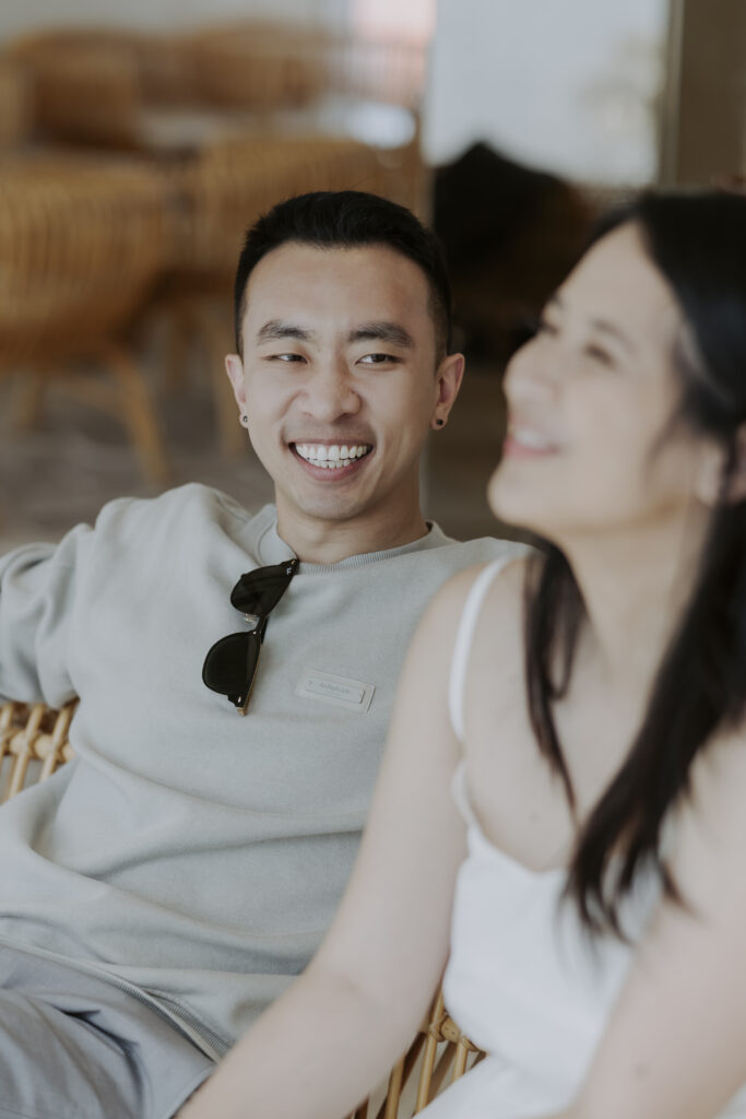 A man and woman smiling while sitting on a wicker chair.