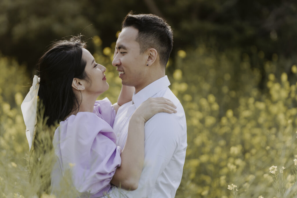 An asian couple embracing in a field of yellow flowers.
