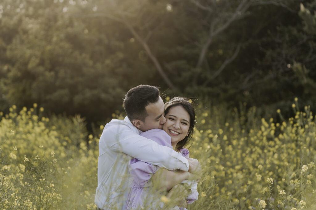 A man and woman hugging in a field of flowers for their pre-wedding outdoor photoshoot