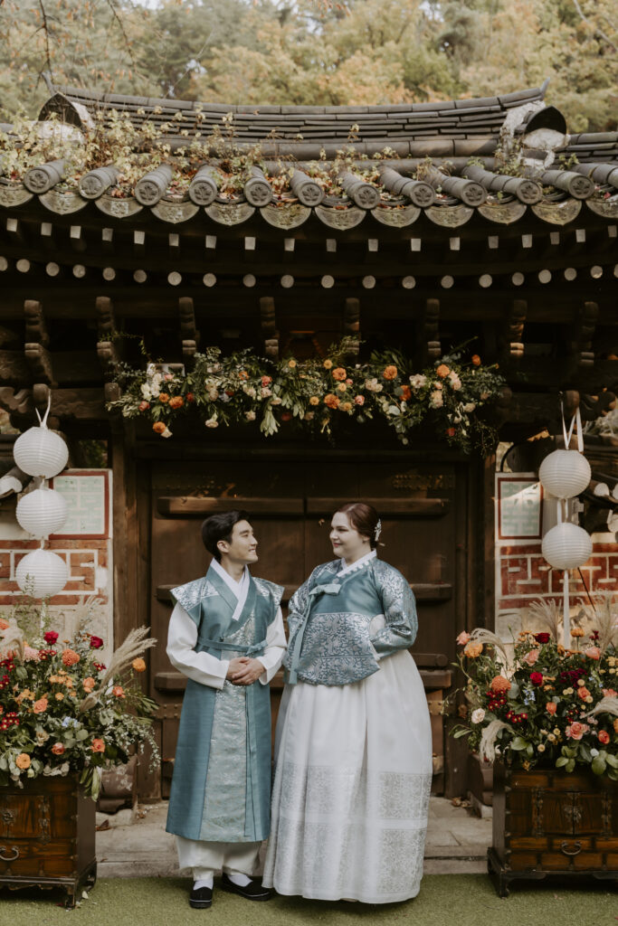 A couple in traditional korean clothing standing in front of a hanok in Seoul.