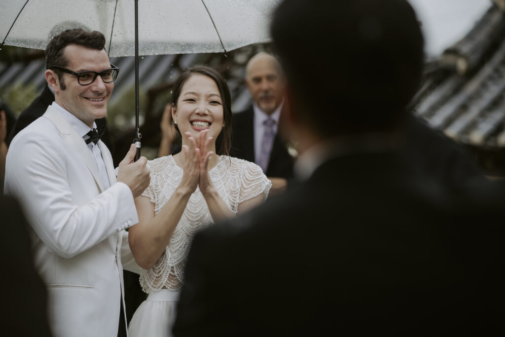 A bride and groom clapping during speeches at their wedding reception in Seoul.