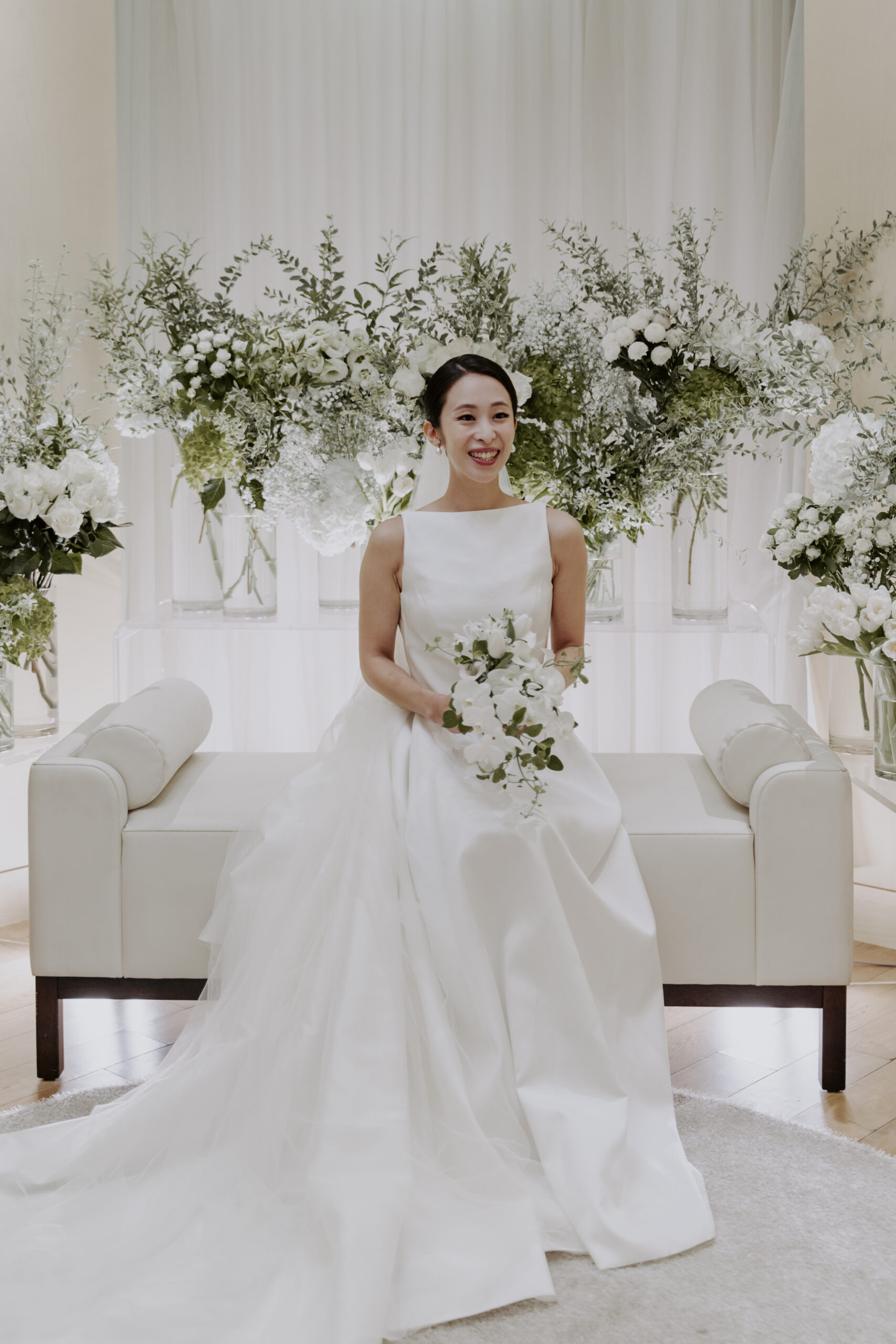 A bride in a white dress sitting on a white couch.