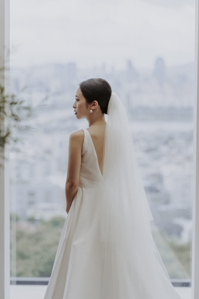 A bride in a white wedding dress standing in front of a window.
