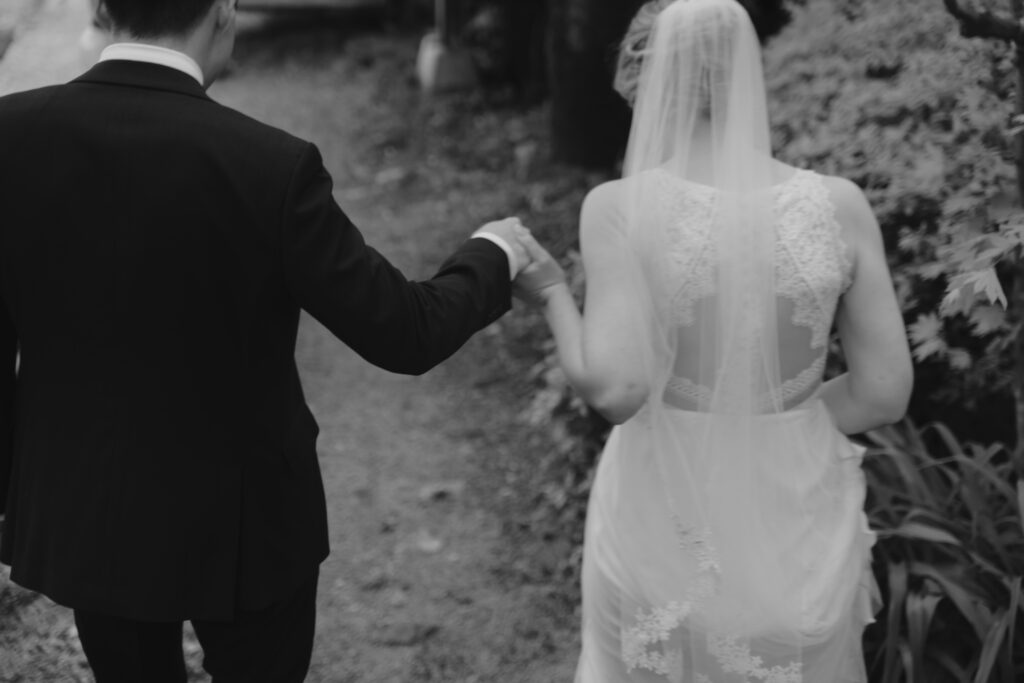A black and white photo of a bride and groom holding hands.