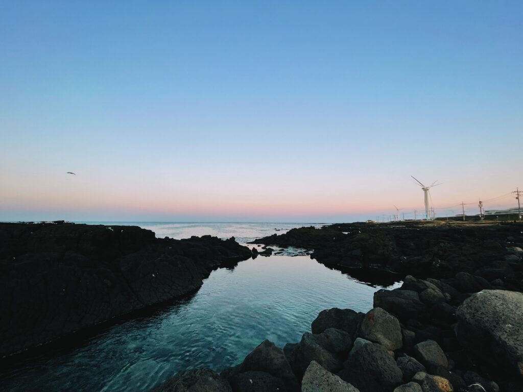 A rocky shore in Korea with wind turbines in the distance.