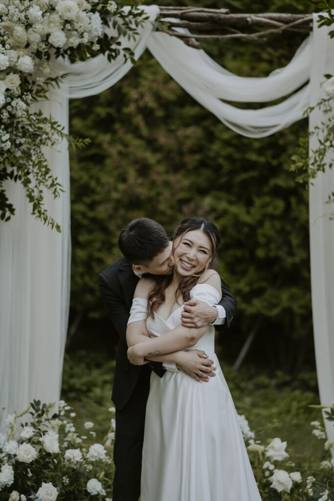 A bride and groom hugging under a wedding arch in Seoul.