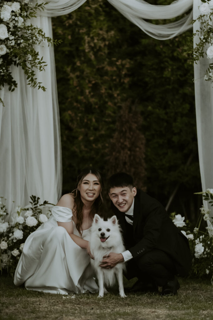 A bride and groom posing for a photo with their dog.