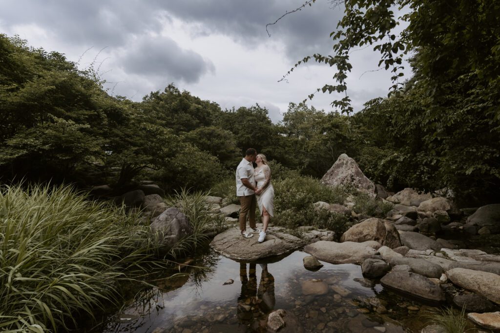 A couple standing on rocks in a pond while looking at each other.
