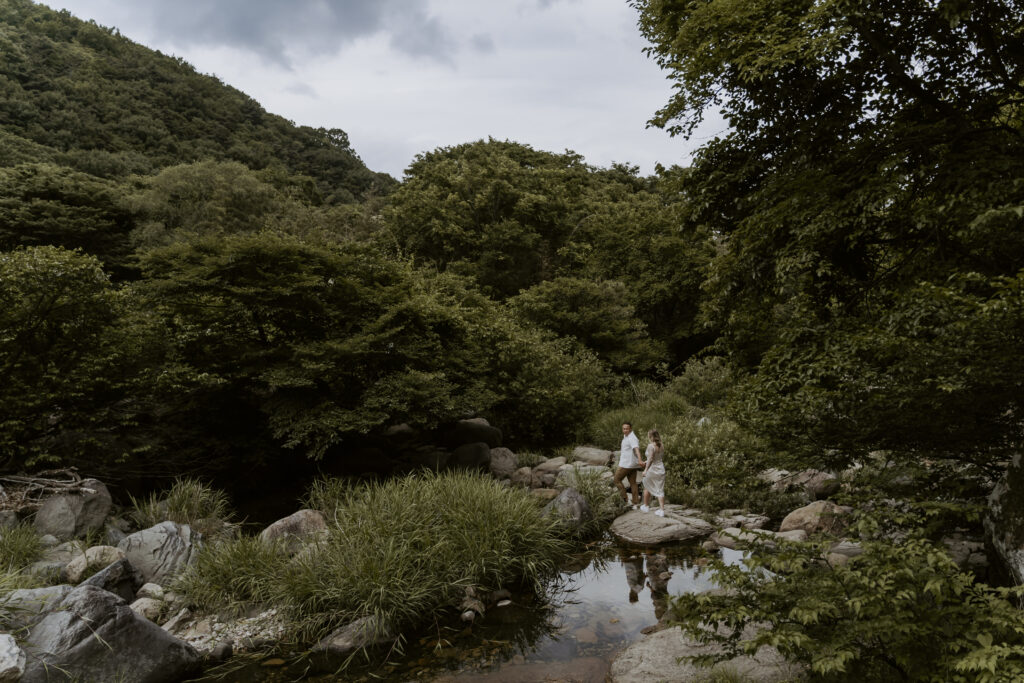 A couple standing on a stream in a wooded area.