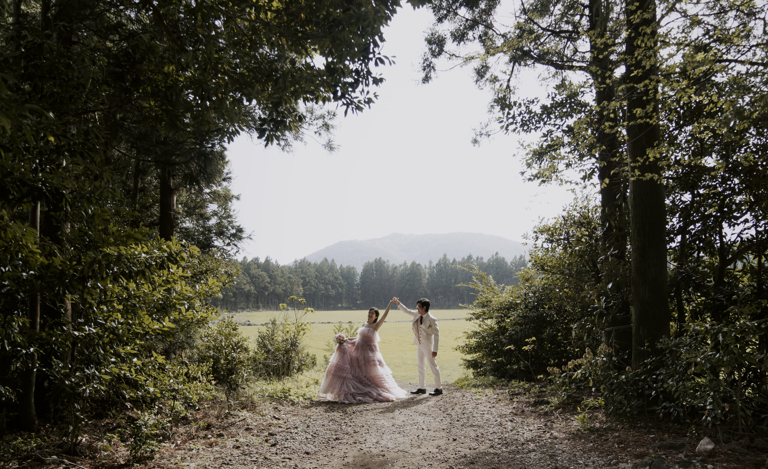 A bride and groom walking down a path in the woods.