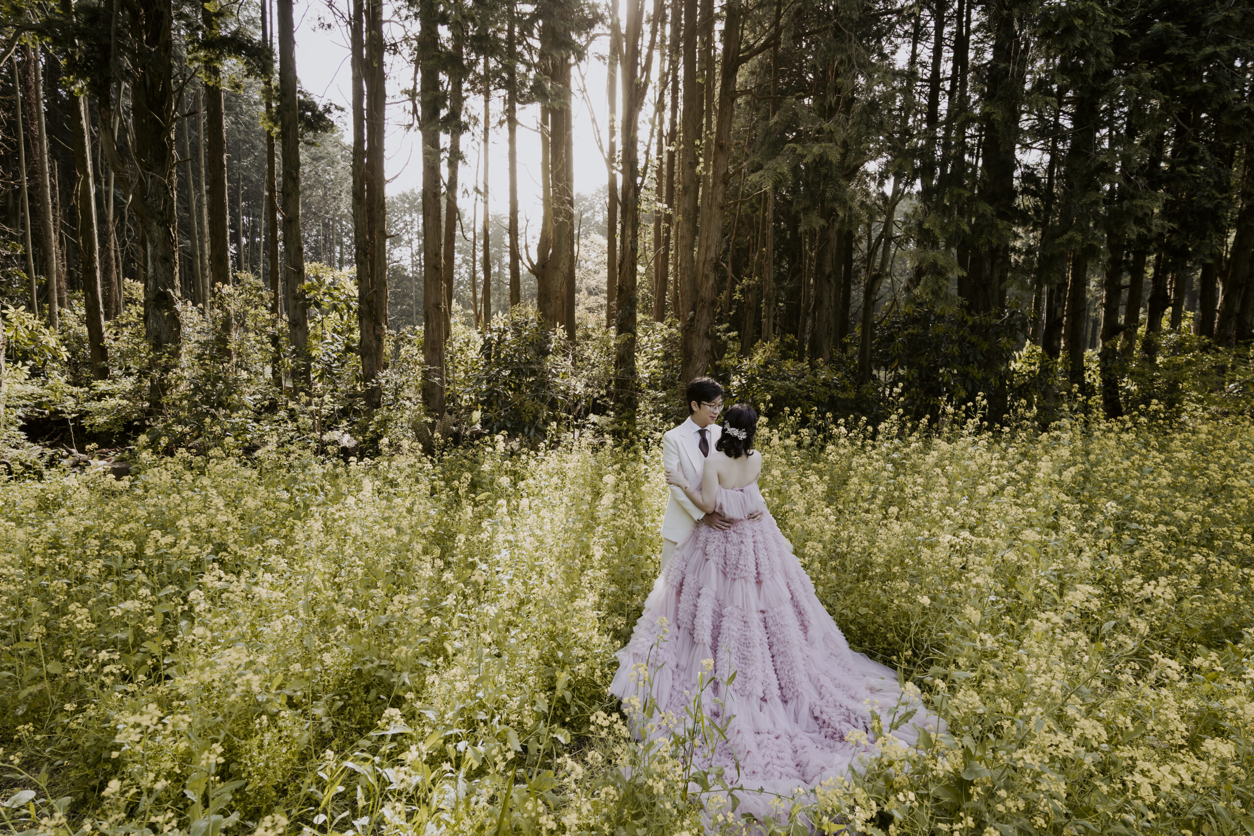A bride and groom enjoying a pre-wedding photoshoot on Jeju Island amidst a field of yellow flowers.