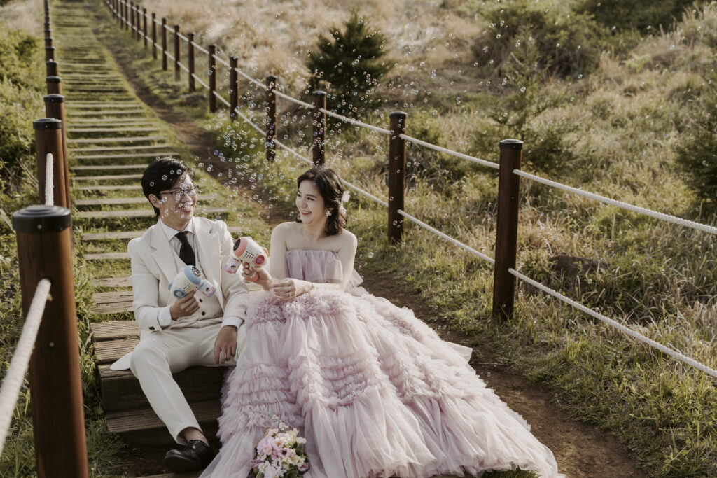 A couple poses for their pre-wedding photoshoot on a wooden walkway on Jeju Island.
