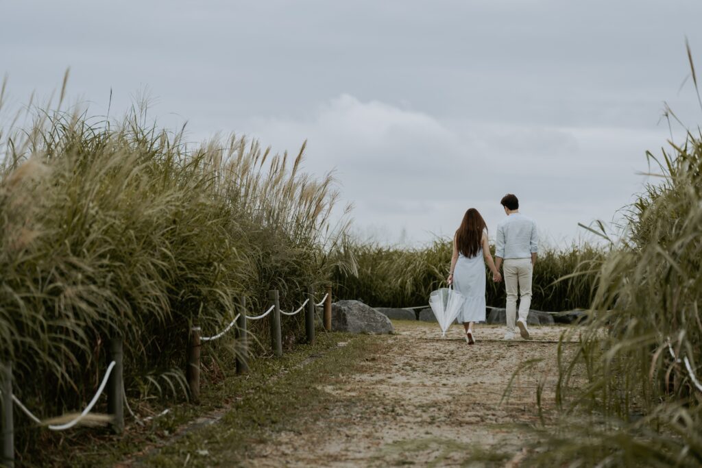 A couple walking down a path with tall grass in the background.