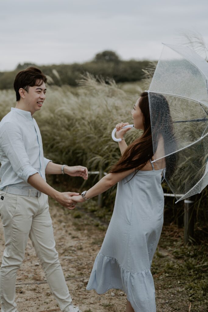 A man and woman holding an umbrella in a field for their pre-wedding shoot Haneul Park, Seoul South Korea. 