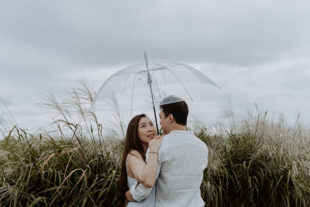An asian couple embracing under an umbrella in a field in Haneul Park, Seoul South Korea