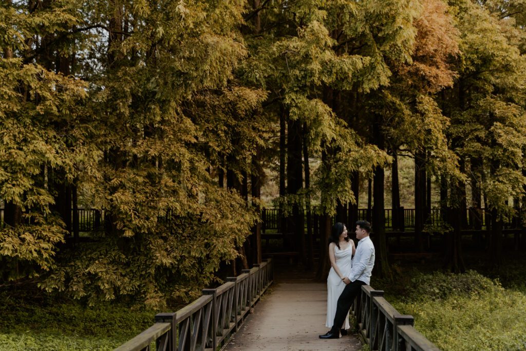 A couple standing on a bridge in a forest.