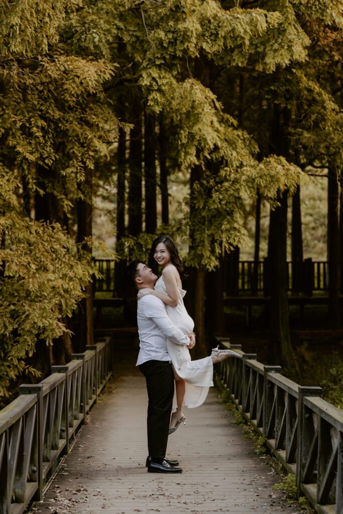 A bride and groom standing on a bridge in the woods.