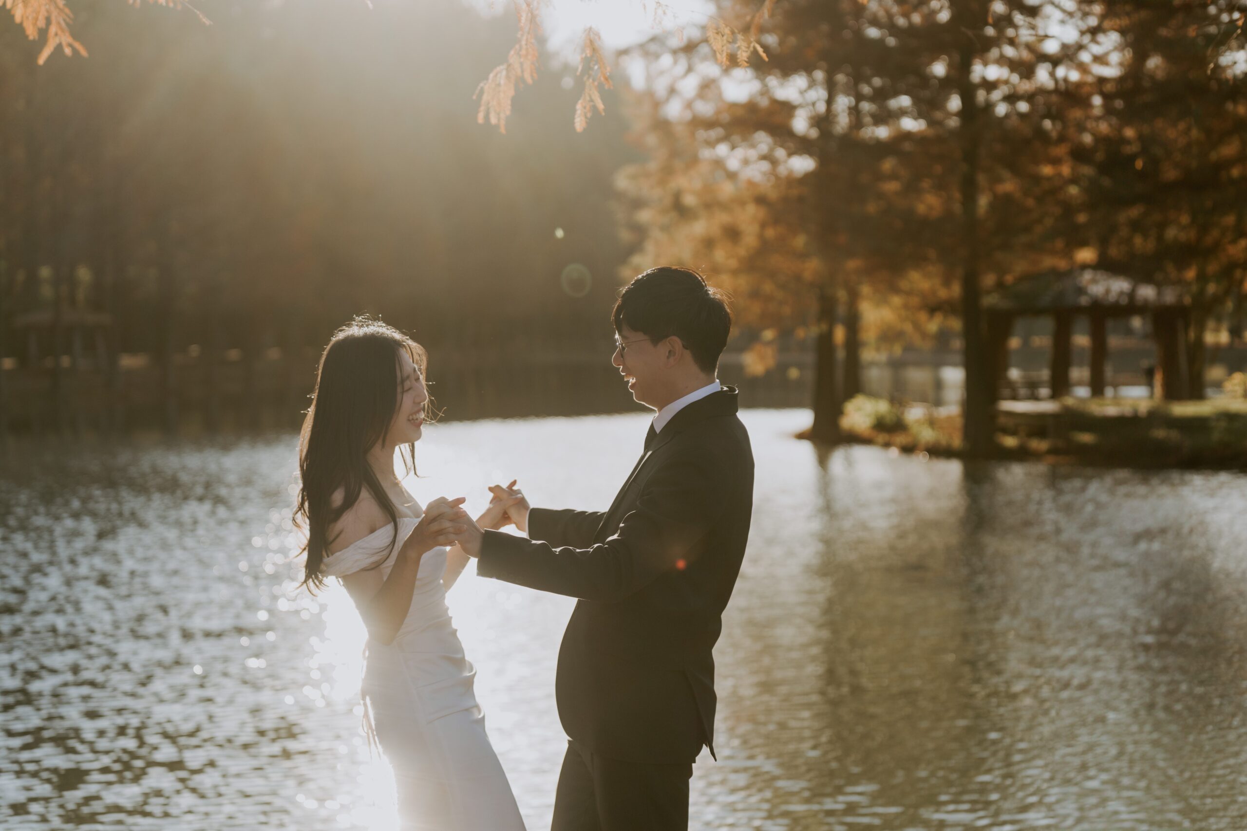 A bride and groom standing in front of a pond.