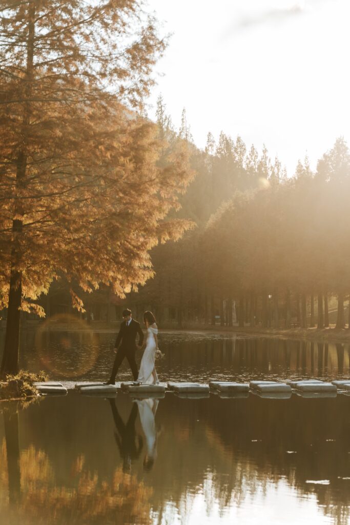A bride and groom standing on a dock near a lake in damyang metasequoia road
