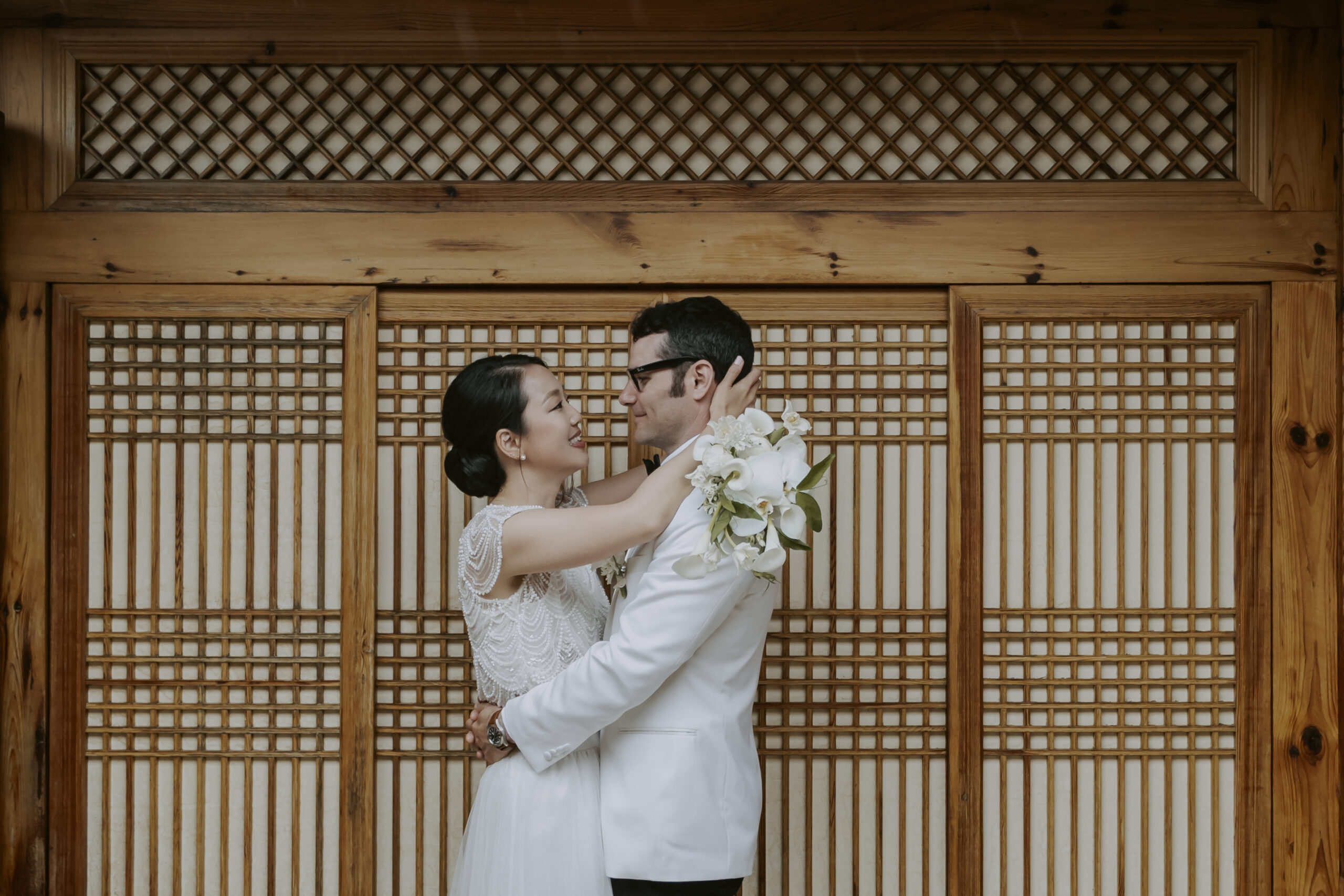 A bride and groom embracing in front of a hanok door at an outdoor wedding in Seoul.