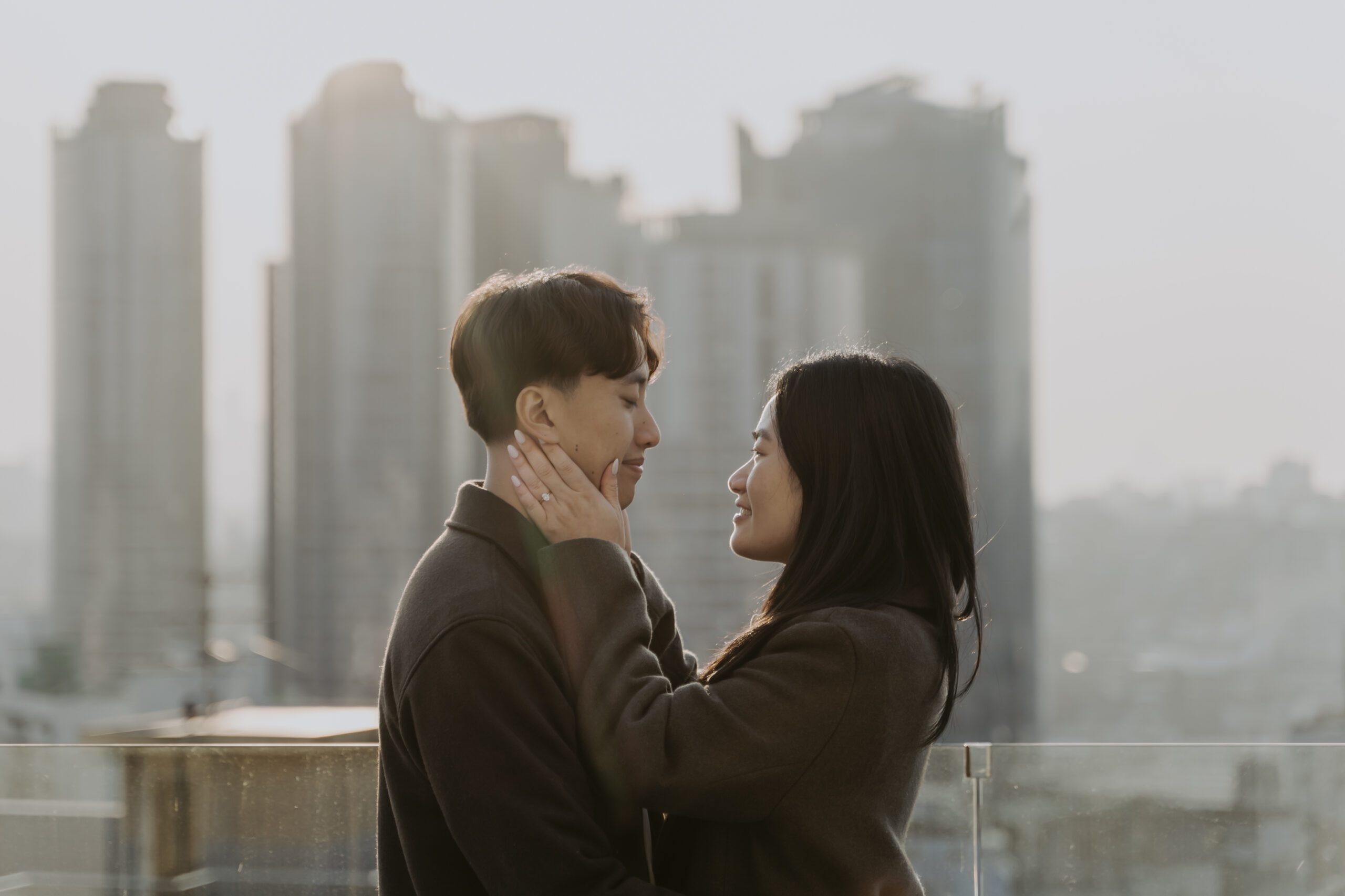 Two individuals sharing a tender moment on a rooftop with cityscape background.