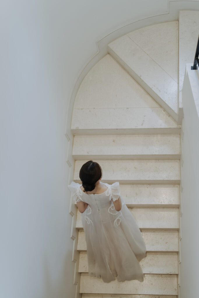 A bride in a white dress is walking up marble stairs. The photo is taken from above.